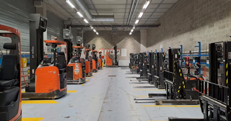 Rang&eacute;e de transpalettes &eacute;lectriques stationn&eacute;s dans une all&eacute;e d'entrep&ocirc;t, &eacute;quipements dont la charge rel&egrave;ve de la rubrique ICPE 2925